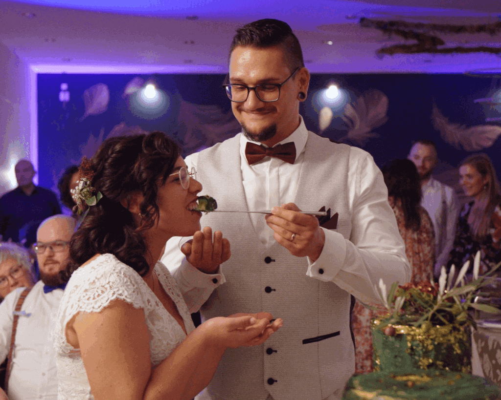 Bräutigam füttert Braut mit Hochzeitstorte, beide grinsen