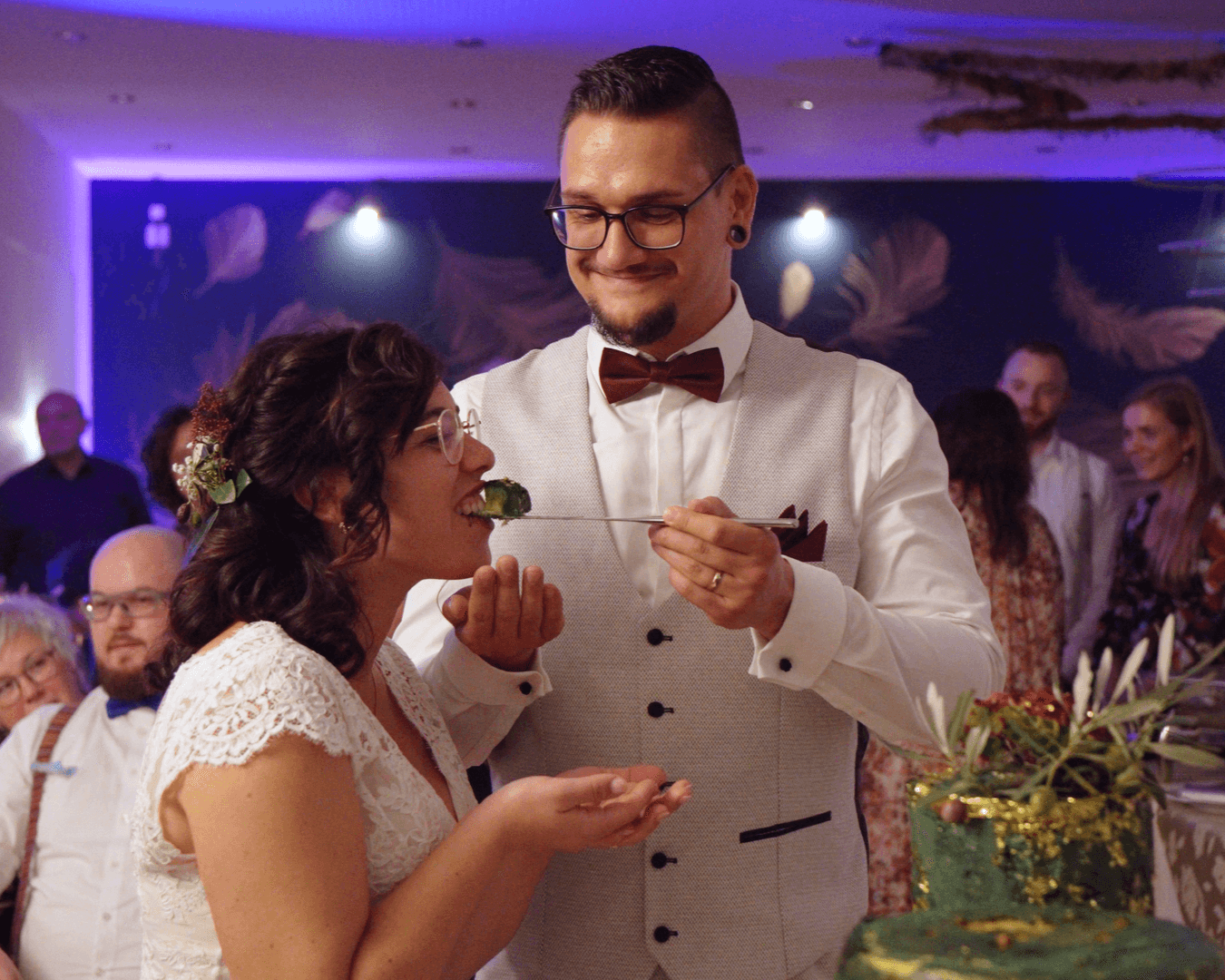 Bräutigam füttert Braut mit Hochzeitstorte, beide grinsen